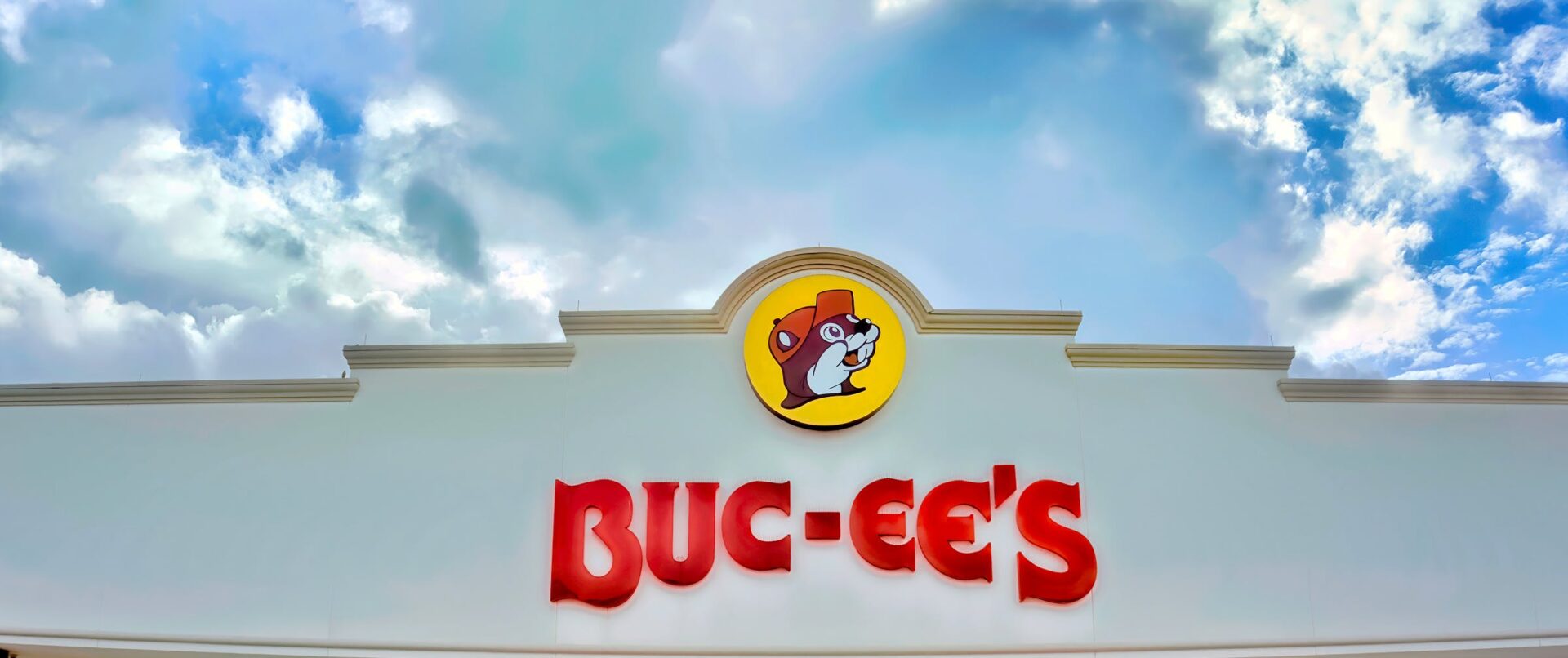 A picture of the building and sign of a Buc-ee's against a blue clouded sky.