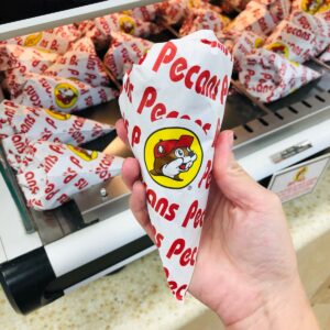 A picture of a hand holding a triangle-shaped bag of pecans with the Buc-ee's logo on the packaging.